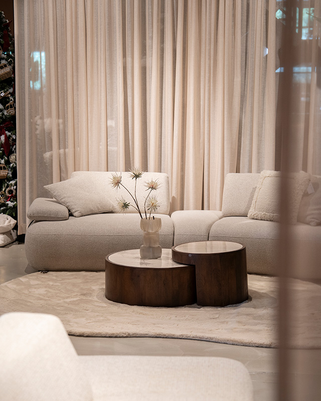 Lichte bank met beige vloerkleed en ronde bruine salontafels in showroom.