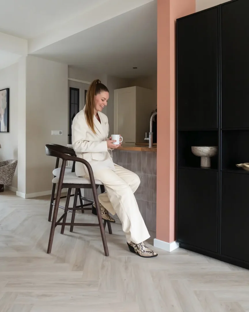 Warme, moderne keukenhoek met een houten barstoel Rayven bruin van het merk Eleonora aan het kookeiland en een marmeren vaas als subtiel decor in de kast