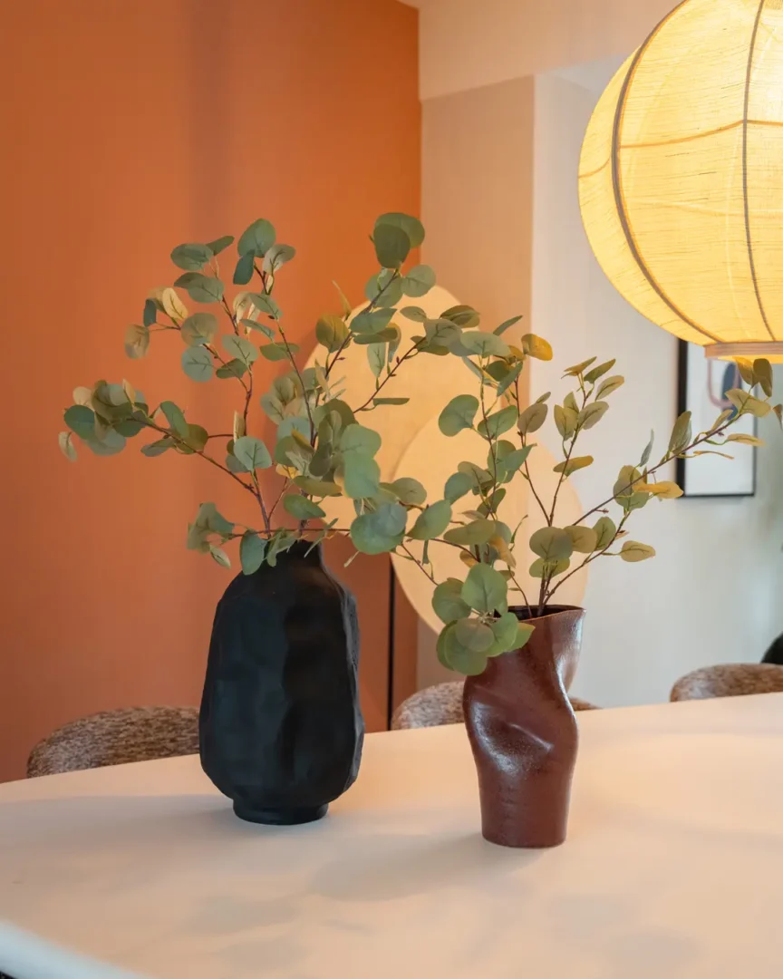 Twee decoratieve vazen in organische vormen met groen blad die een stijlvolle, warme sfeer creëren in het interieur. Songa small - burgundy van By-Boo en Dent large - black van By-Boo.