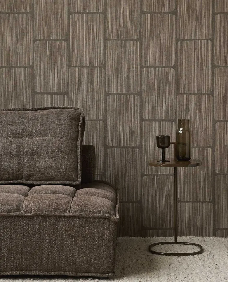 Bruine bank met bijzettafel en donker glaswerk voor een wand met grafisch patroon behang in een moderne, rustige woonruimte.