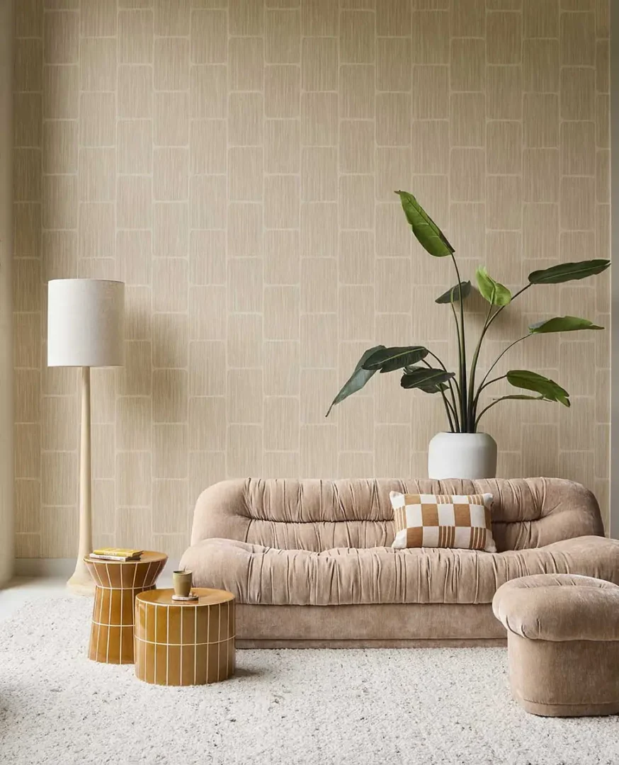 Beige, zachte bank met hocker en houten bijzettafels naast een vloerlamp en grote plant in een moderne, rustige woonruimte.