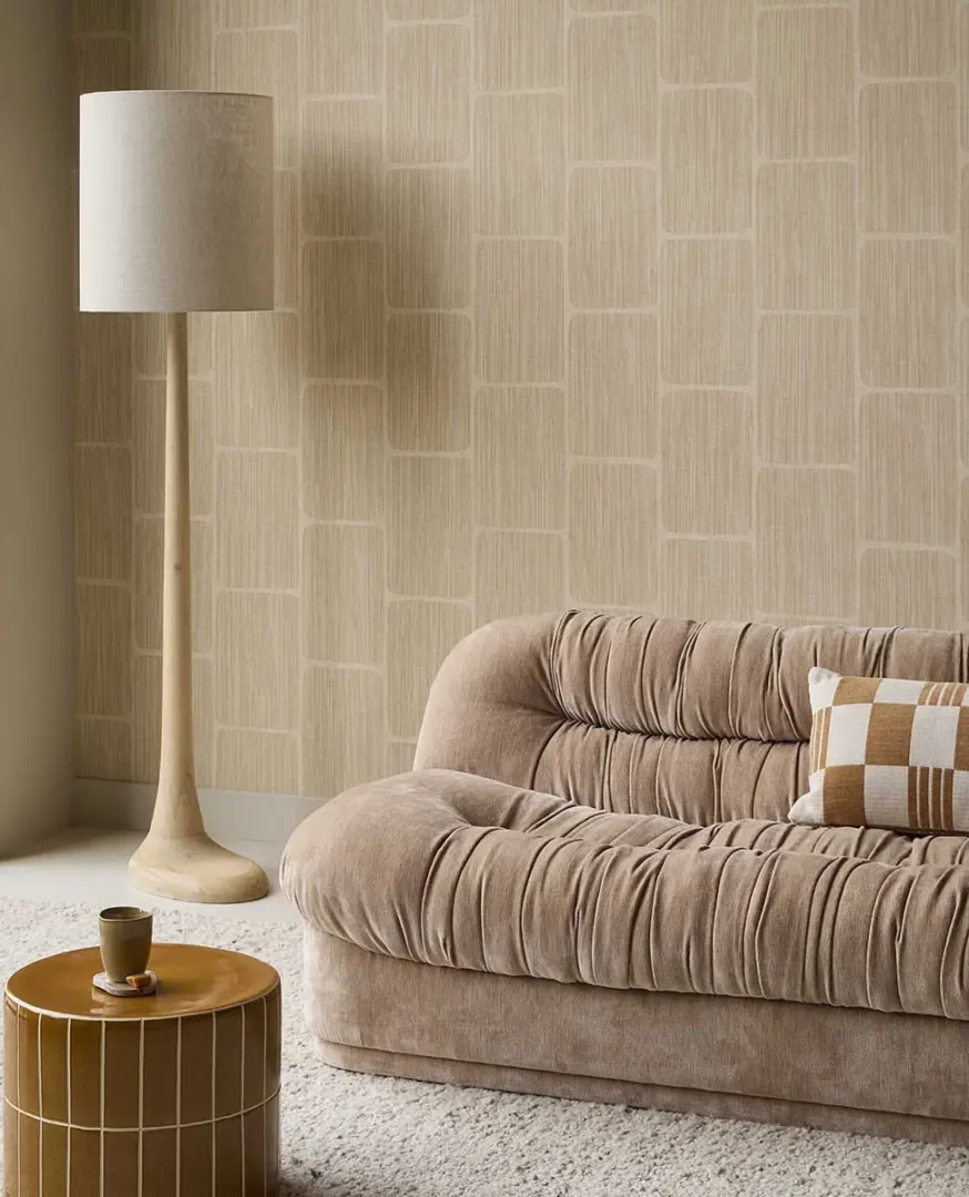 Beige bank met kussen naast een houten vloerlamp en ronde bijzettafel in een rustige, moderne woonhoek.