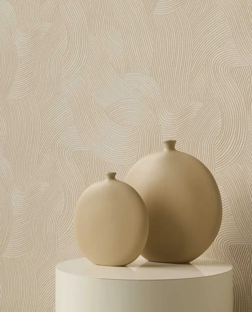 Twee matte beige keramische vazen op een lichte cilindervormige ondergrond voor een wand met golvend reliëfpatroon.