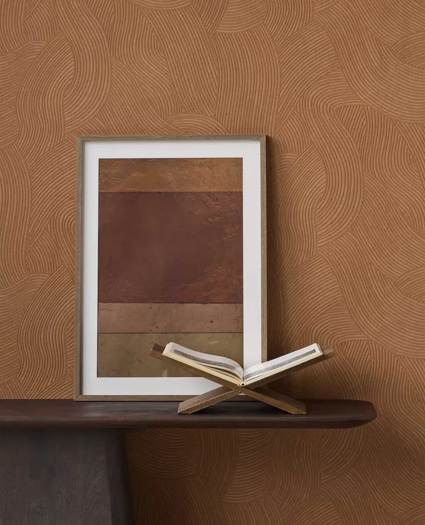 Ingelijste abstracte print en open boek op een houten standaard voor een wand met subtiel golvend patroon.