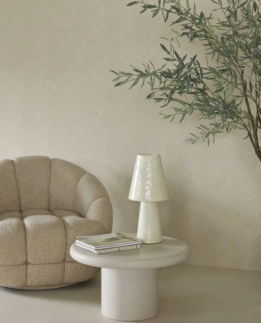Beige, ronde fauteuil naast een lichte bijzettafel met keramische lamp in een rustige, moderne woonhoek.
