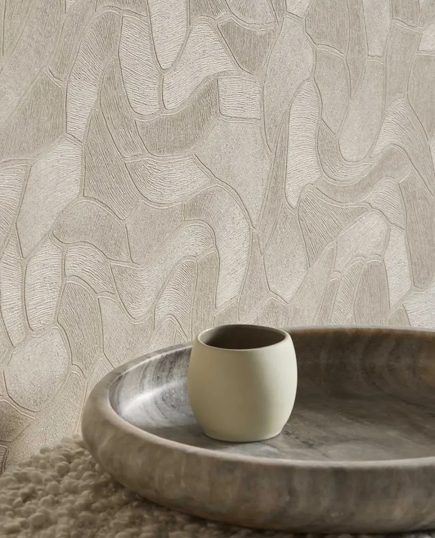 Keramische beker in een stenen schaal die een serene, tactiele sfeer creëert tegen een wand met zacht organisch patroon.