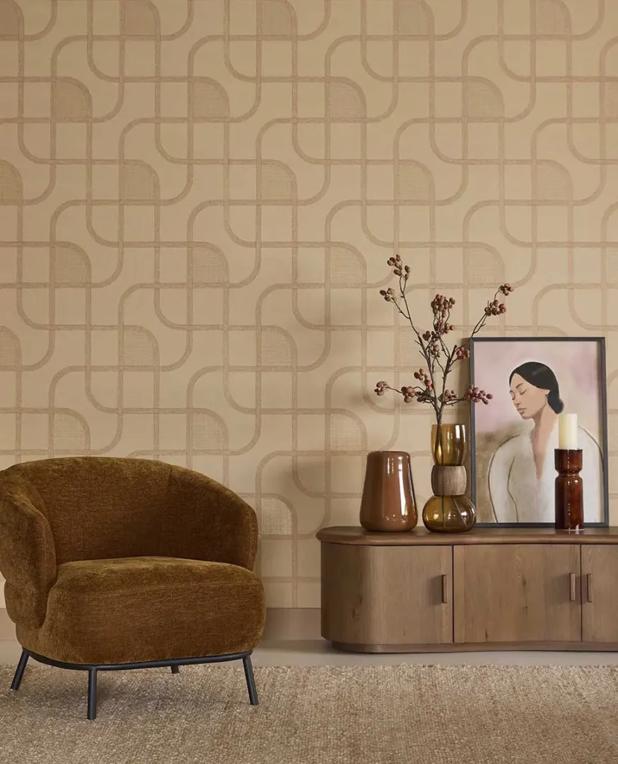 Bruine fauteuil op een licht vloerkleed naast een houten dressoir met keramische en glazen decoratie in een moderne, warme woonruimte.