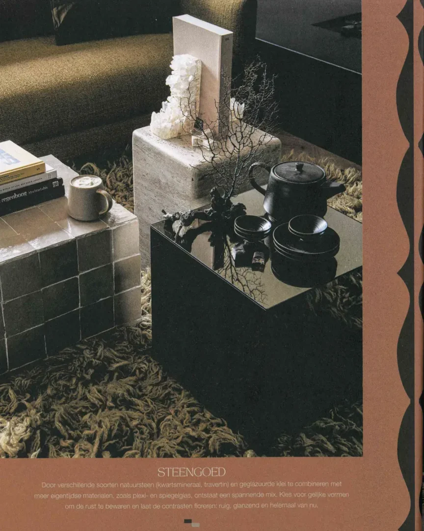 Compositie van drie salontafels in natuursteen, keramiek en glanzend zwart, met een teapot, boeken en kristal op een zacht vloerkleed.