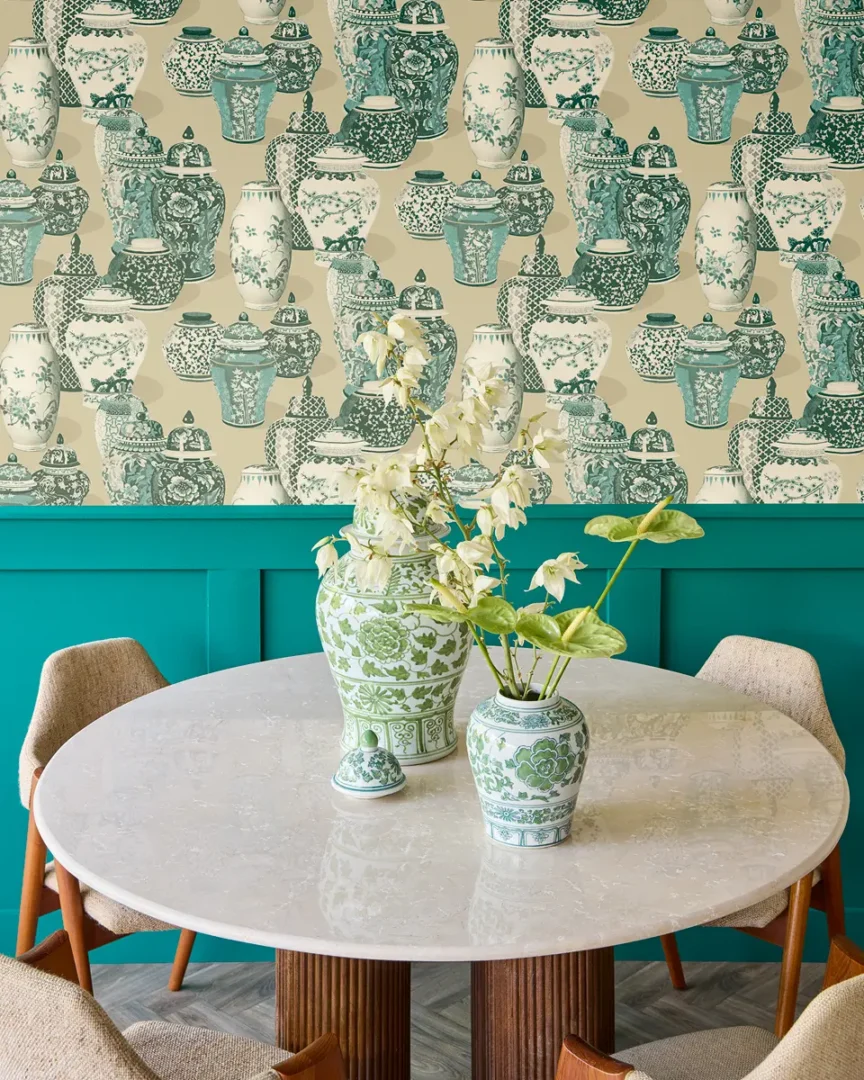 Eetkamer met ronde marmeren tafel, groene keramische vazen met bloemen en behang vol vazenmotieven in turquoise tinten.