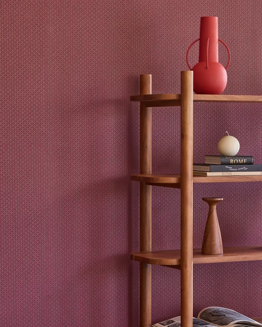 Interieurhoek met houten rek tegen een rode geometrische wand, met boeken, keramiek en een matte rode vaas als accent.