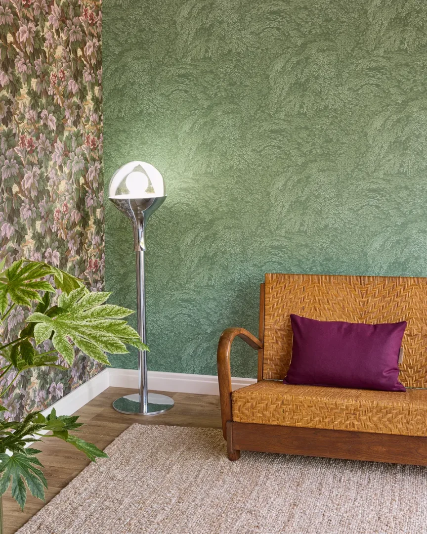 Interieurhoek met rotan bank, paarse kussen, groene wand en bloemrijk behang, verlicht door een retro chromen vloerlamp.