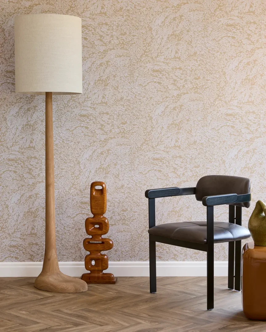 Interieurhoek met houten vloerlamp, sculpturale houten objecten en een moderne stoel tegen een beige gemarmerde wand.
