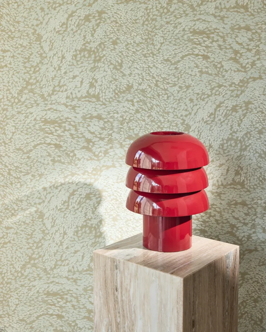 Minimalistische compositie met glanzende rode sculptuurvaas op een lichte houten sokkel tegen een beige gemarmerde wand.