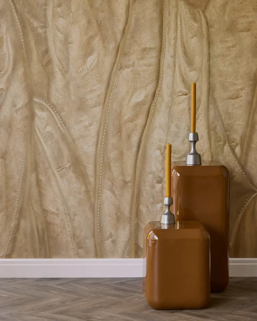 Interieurhoek met beige wand met organische textuur, twee glanzende bruine kandelaars met gele kaarsen en visgraatvloer.
