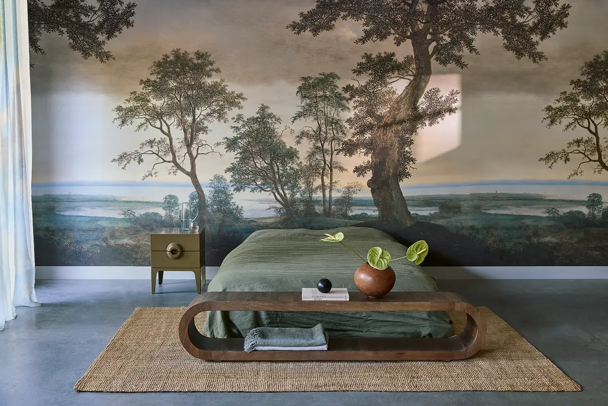 Slaapkamer met wand vol landschapprint, houten bank, olijfgroen beddengoed en aardse accessoires in een serene, natuurlijke setting.
