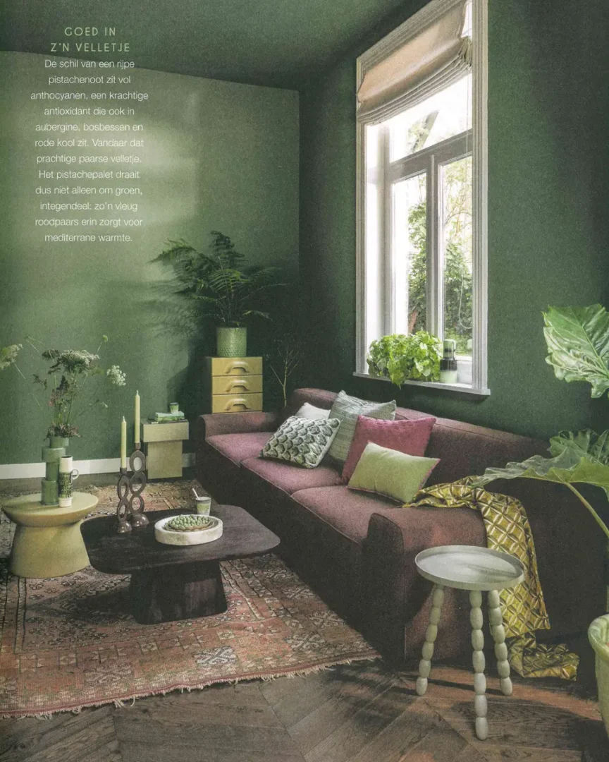 Groene woonkamer met paarse bank, planten, houten tafels en een oosters vloerkleed dat warmte en diepte toevoegt.