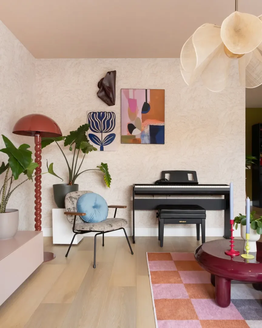 Creatieve woonkamerhoek met digitale piano, abstracte kunst aan de wand, rode vloerlamp, designstoel en roze‑oranje vloerkleed.